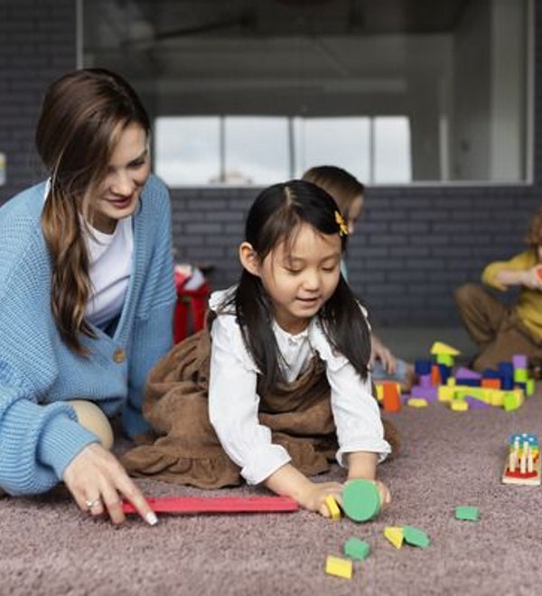 Teacher kneeling on the floor playing alongside a young girl at Super Kidz Club