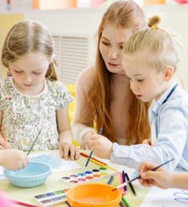 Teacher painting at a table with two young children